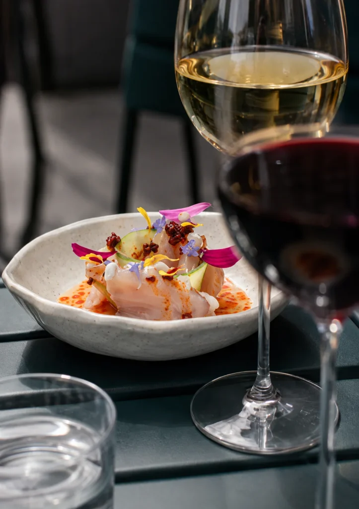 Glasses of white and red wine beside a small seafood dish with edible flowers