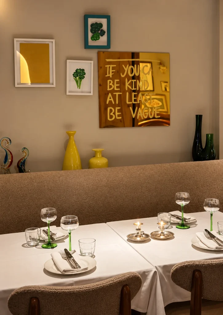 Dining room with white tablecloths, green glassware and a gold mirror sign