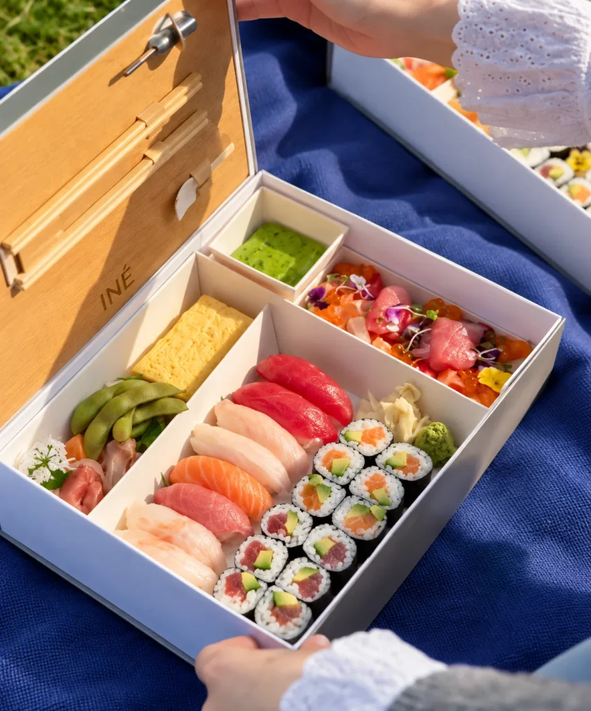 Bento box of sushi and sashimi on a blue picnic blanket