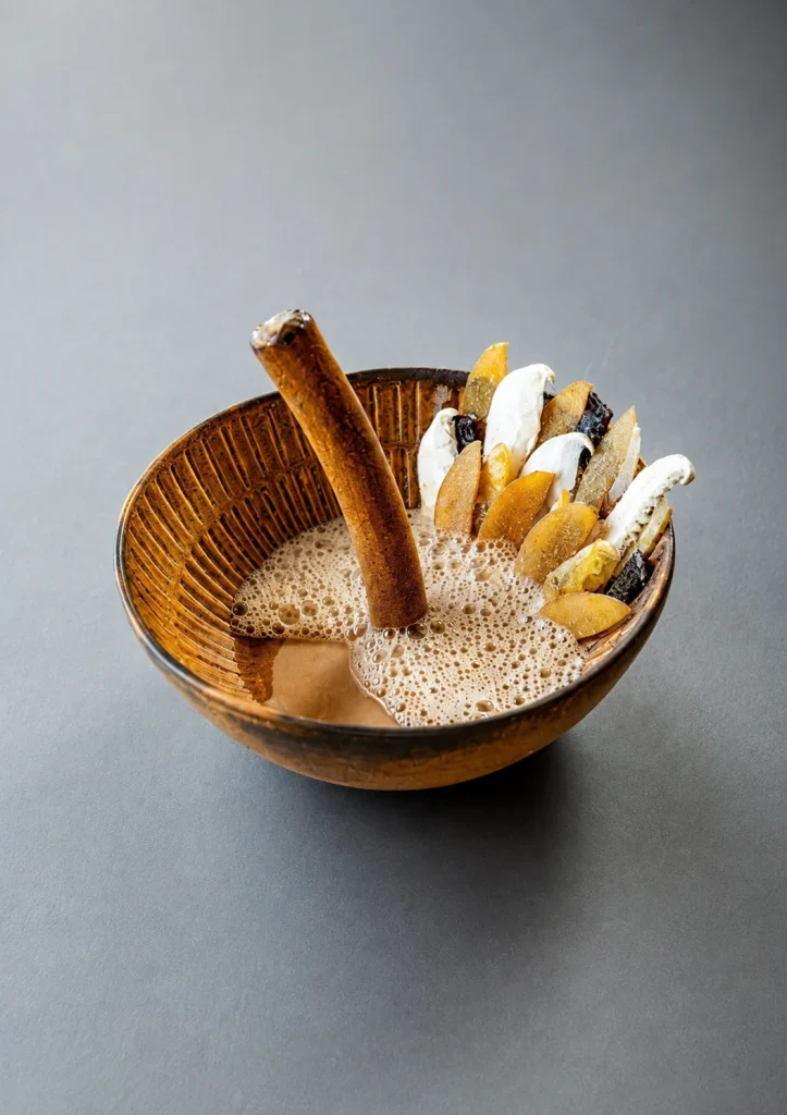 Wooden bowl of dessert topped with sliced banana and a cinnamon stick